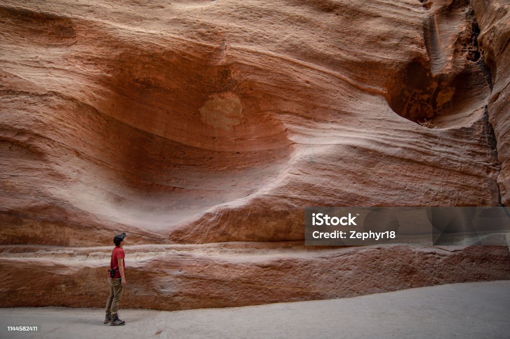 Asian man traveler and photographer standing in the Siq, the narrow slot-canyon that serves as the entrance passage to the hidden city of Petra, Jordan. Travel Middle East concept Adult Stock Photo
