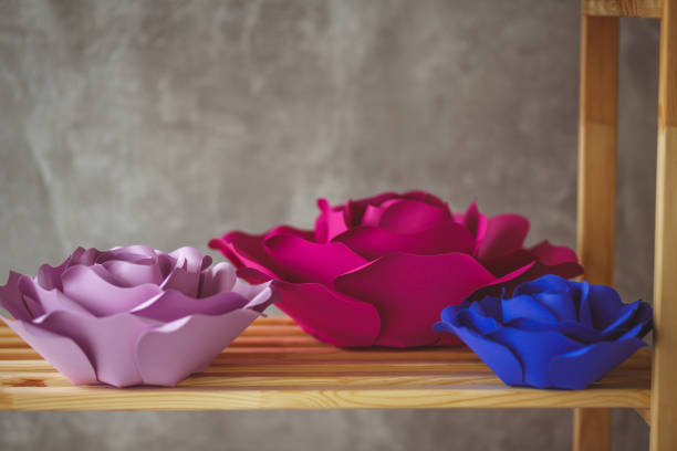 Pink and blue paper flowers sitting on wooden shelf.
