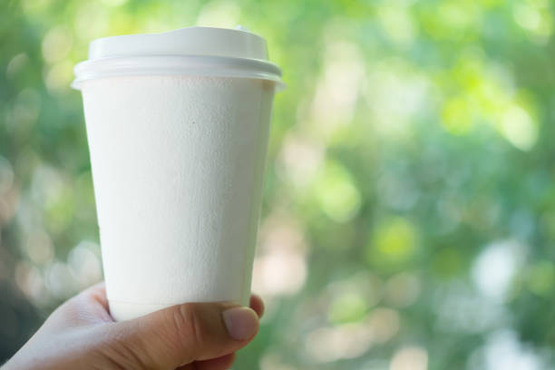 istock Blank white paper coffee cup mockup in hand. Disposable cup template design with no branding. 1144582973