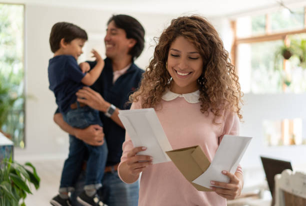 Beautiful young mother looking at the mail while dad and son play at background