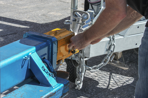 Man fastening a chain onto an industrial hitch on a trailer - close-up