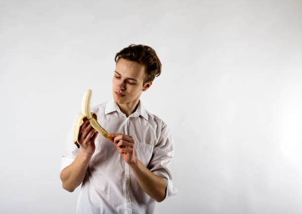 istock Young man in white is holding a banana. 1144596626