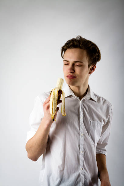 istock Young man in white is holding a banana. 1144596679