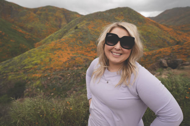 linda mujer rubia que lleva gafas de sol y ropa casual posa en walker canyon con colinas cubiertas de amapola en el fondo - flower red poppy sky fotografías e imágenes de stock