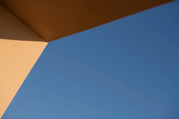 Architectural detail of yellow concrete wall and clear blue sky in morning sunlight making geometric pattern. Shallow depth of field.