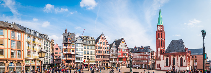 Crowds of tourists in the Romerberg square overlooked by the medieval townhouses, cafes and restaurants of the Altstadt Old Town and spire of Alte Nikolaikirche in the heart of Frankfurt, Hesse, Germany.