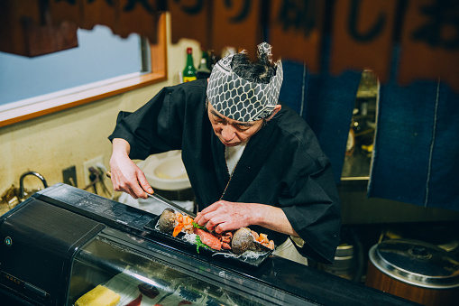 A real Japanese Sushi chef prepares sushi for his restaurant in Tokyo, Japan. He prepares sushi, known as nigiri, for dinner. This traditional Japanese food is being prepared on a wooden platter.