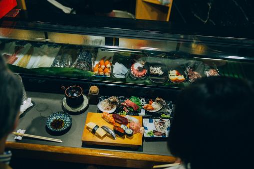 A mature couple, a Japanese man and woman eat sushi at a sushi restaurant in Tokyo, Japan. There is selection of nigiri sushi on the bar in front of the customers, high angle view.