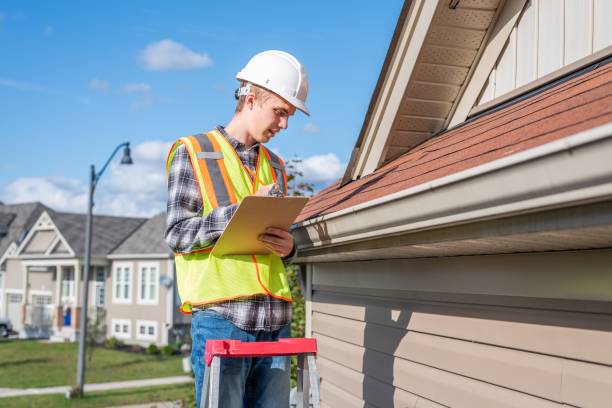 Home inspector providing an inspection to a house. The image displays a home inspector standing on a ladder and providing an inspection to the roof of a house. He is dressed in safety gear. inspector stock pictures, royalty-free photos & images