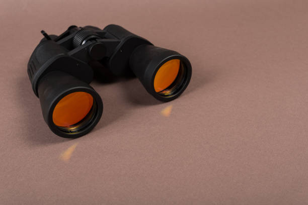 istock Black binoculars with orange lens on pastel background 1144619249