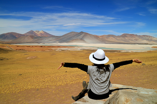 Woman Raising Her Arms In Front of Awesome View of Salar de Talar salt Lakes and Cerro Medano Mountain, Chilean Andes, Northern Chile