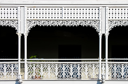 Victorian decorative wrought iron balcony with a plant on it but mostly darkness behind the white painted ornate railings - background