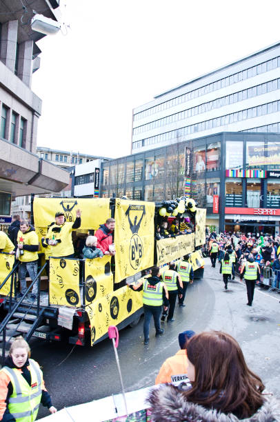 le personnel de sécurité, les touristes et les habitants (y compris les enfants) devant le train de parade du club à dortmund munder rosenmontag (rose lundi) carnaval, sur kampstrasse, allemagne. - football police officer crowd photos et images de collection