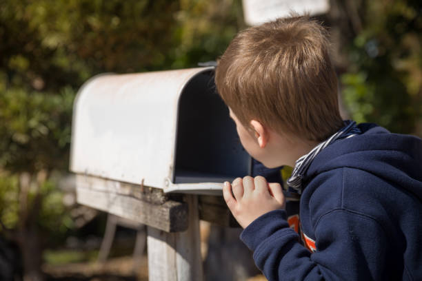 school boy opening a post box and checking mail. kid waiting for a letter, checking correspondence and looking into the in the metal mailbox. - looking into mailbox imagens e fotografias de stock