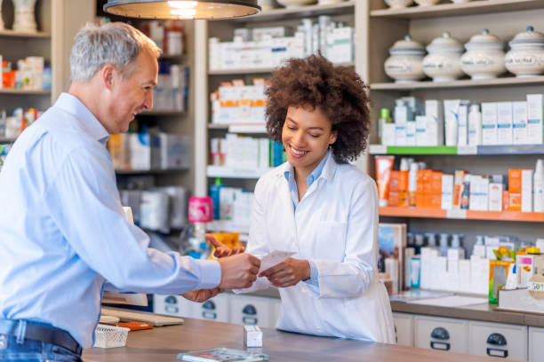 Let us help you fight the winter blues! Photo of female mixed race Pharmacist giving prescriptions of medicine to mature gray hair customer in pharmacy. Female pharmacist showing medicine to male customer in pharmacy. Chemist suggesting medical drug to buyer in pharmacy drugstore. retail clerk photos stock pictures, royalty-free photos & images