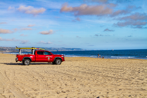 Newport Beach, CA / USA – April 6, 2019: Newport Beach Fire Department Lifeguard truck on beach near the Balboa Peninsula facing the shoreline of Pacific Ocean while people enjoy the beach.