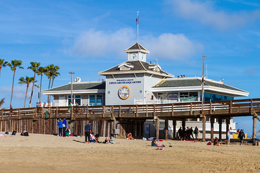 Newport Beach, CA / USA – April 6, 2019: People enjoying a day at the beach with the Newport Beach Lifeguard Headquarters in the background located on the pier in Newport Beach, California.