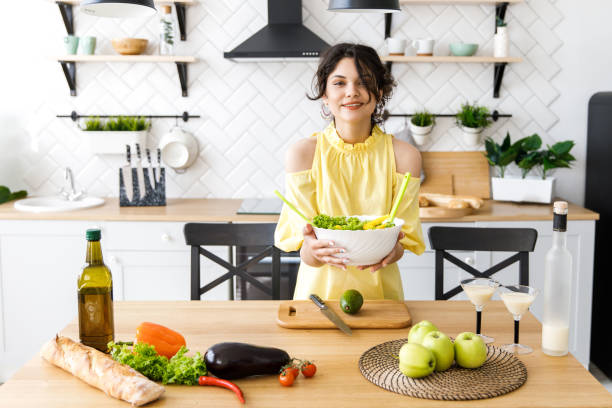 junge hübsche frau schneidet eine avocado auf einem hölzernen salatbrett. kochen. zubereitung von frischem gemüsesalat - dressing room women female adult stock-fotos und bilder