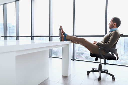 Businessman sitting with legs up on desk viewing city relaxing after close a deal