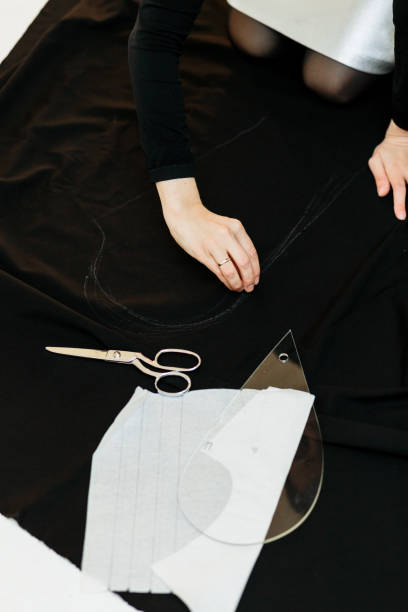 istock Beautiful seamstress, cut black fabric on the studio floor 1144641405