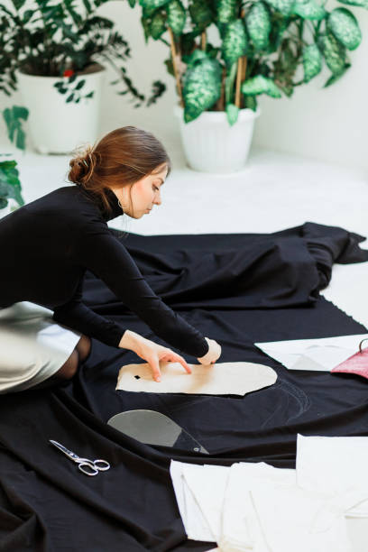 istock Beautiful seamstress, cut black fabric on the studio floor 1144642439