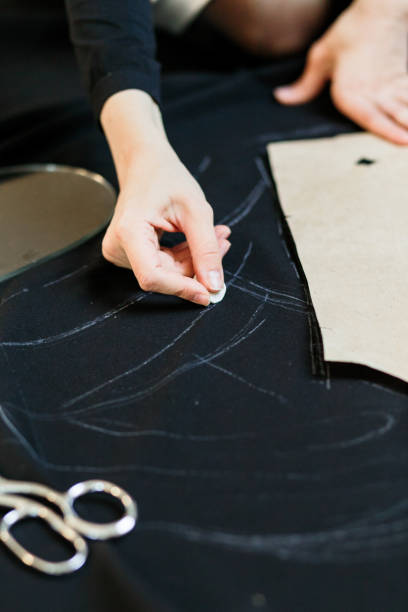 istock Beautiful seamstress, cut black fabric on the studio floor 1144642596