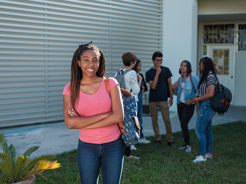 A beautiful afro-caribbean young female standing with arms crossed on a college campus looking at the camera smiling.