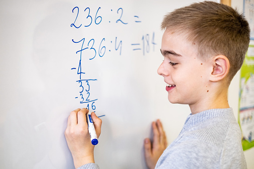 Profile view boy counting on white board in classroom