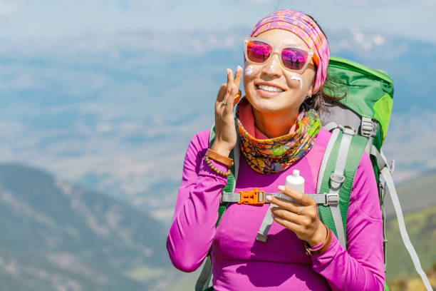 mulher do caminhante que aplica o creme do sol para proteger sua pele dos raios uv perigosos do sol elevados nas montanhas. conceito dos cuidados médicos do curso - roupa desportiva de protecção - fotografias e filmes do acervo