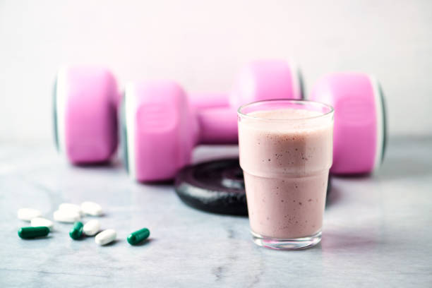 glass of protein shake with milk and raspberries. bcaa amino acids, l - carnitine capsules and pink dumbbells in background. sport nutrition. stone / wooden background. copy space. - body building milk shake protein drink drink imagens e fotografias de stock