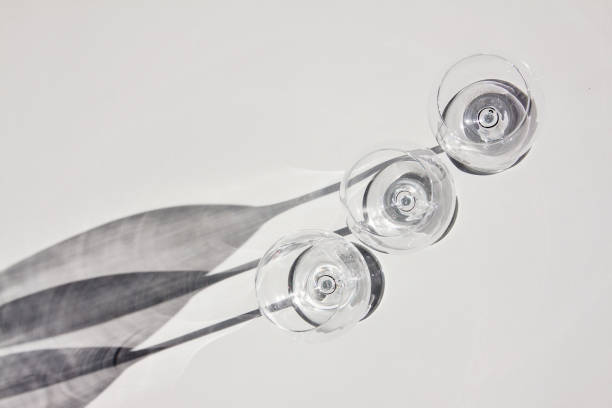 Row of three wine glasses. Abstract shadows, sunlight, white background.