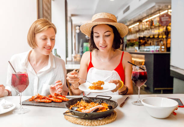 Dos alegres amigas chicas bebiendo vino y almorzando en el restaurante de mariscos - foto de stock