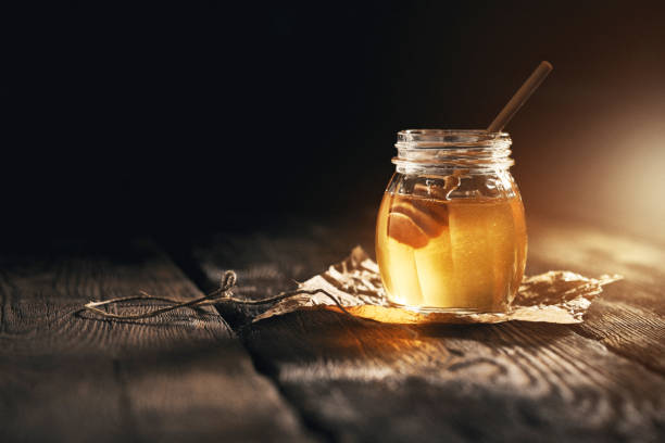 Jar of camomile honey on black background Jar of camomile honey on black background with bamboo dipper on wooden table. honey jar liquid gourmet stock pictures, royalty-free photos & images