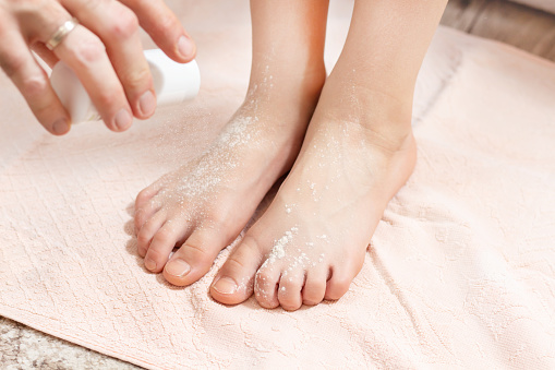 the male hand holds the container with the powder and pour the white powder on child's feet. Medicine against sweating of the feet.