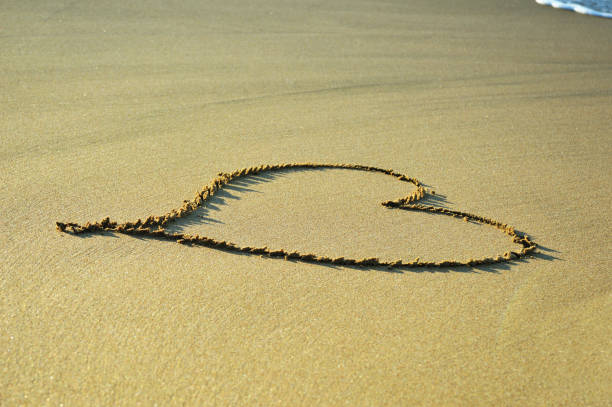 istock Drawing heart symbol on the sand background at the beach 1144655818