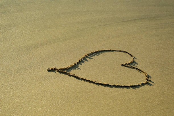 istock Drawing heart symbol on the sand background at the beach 1144656787
