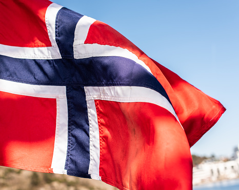 The flag of the United Kingdom of Great Britain and Northern Ireland, known as Union Flag or Union Jack, hanging down loosely at full-mast on a white pole against blue sky.