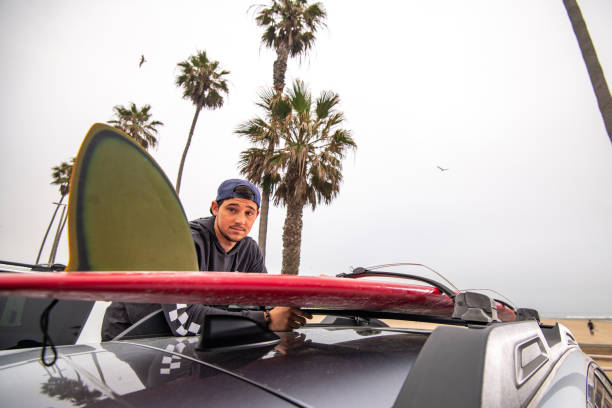 istock Surfer Stands on Car To Unload Surfboard off The Roofrack 1144659341