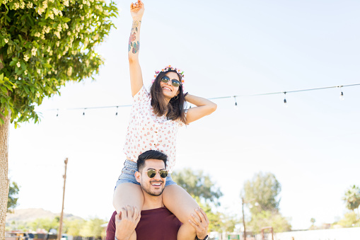 Attractive woman dancing to music while sitting on shoulders of boyfriend at outdoor party