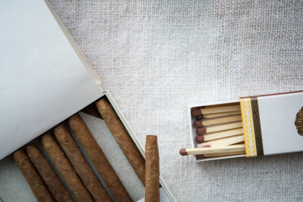 Cigars and whiskey on a light table cloth, one cigar out of the packet