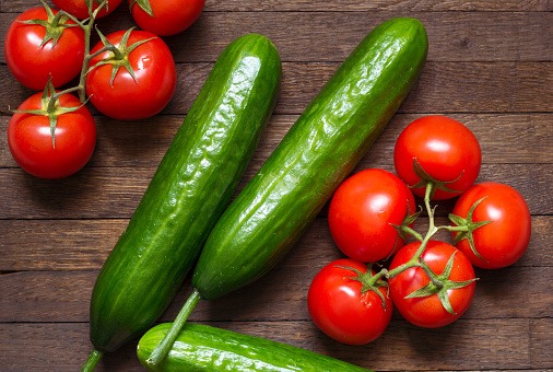 Red ripe tomatoes on branch and big green cucumbers on wooden background. Agriculture background. Vegetables laid on burnt oak desk. Raw foods. Healthy nutrition concept. Crop plant. Top view close up