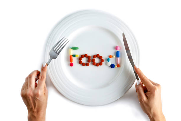 istock Young woman hands with fork and knife ready to eat. Dinner plate assorted pills and capsules forming food word or sign. 1144673707