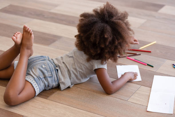 istock Back view african little girl drawing lying on warm floor 1144680168
