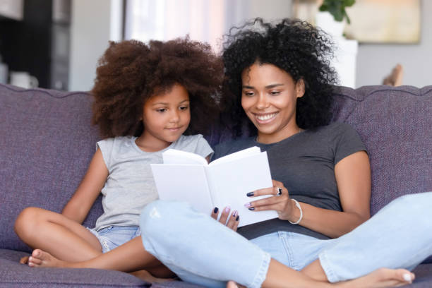 istock African mother and little daughter sitting on couch reading book 1144680176