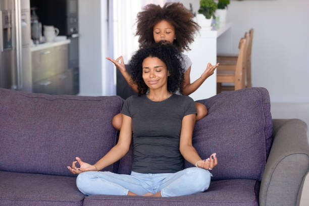 madre africana e figlia piccola meditando sul divano di casa - african descent american culture exercising women foto e immagini stock