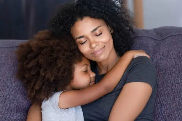 Photo of Closeup african daughter embracing mother sitting on couch at home