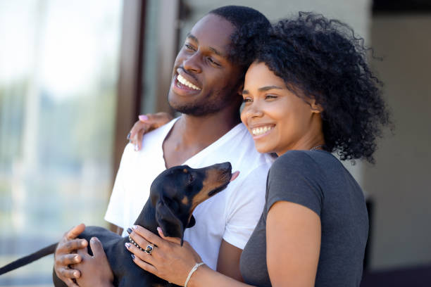 Happy african millennial couple standing outdoors holding dachshund puppy