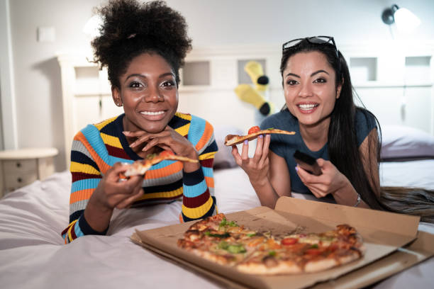 istock Girlfriends eating pizza in bed and watching TV 1144711970