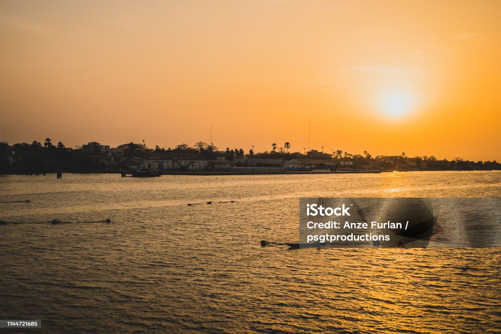 Sunset in ziguinchor. Sunset in Ziguinchor, Africa, observing it from the bridge over casamance river looking towards the ferry port. A fisherman with boat and nets are seen in the picture. Beach Stock Photo