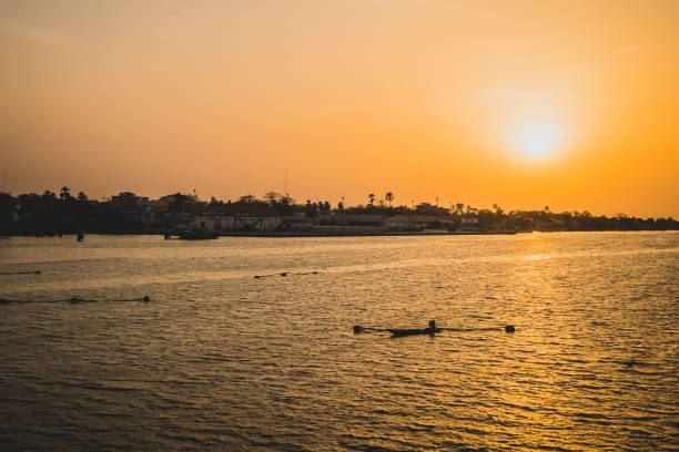 Sunset in ziguinchor. Sunset in Ziguinchor, Africa, observing it from the bridge over casamance river looking towards the ferry port. A fisherman with boat and nets are seen in the picture. casamance river stock pictures, royalty-free photos & images